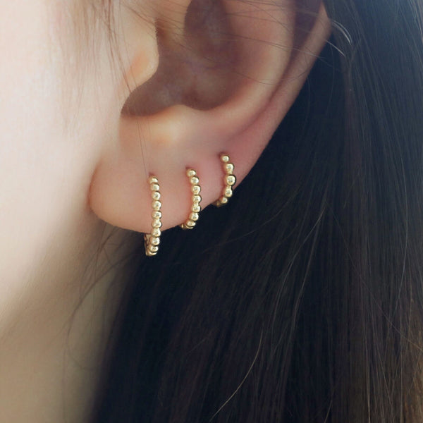 stacked triple lobe piercings featuring beaded huggie hoop earrings